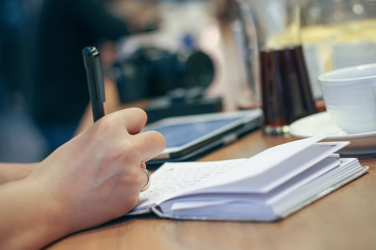 Datum, Uhrzeit und URL zu jedem Screenshot zu notieren macht Beweise vor Gericht verwertbar. hand writing notes in paper notebook on desk, daylight