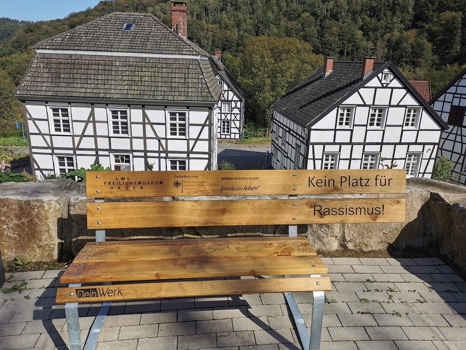 مقعد خشبي كُتب عليه بالألمانية "Kein Platz für Rassismus" أمام بيوت تقليدية في متحف Hagen المفتوح