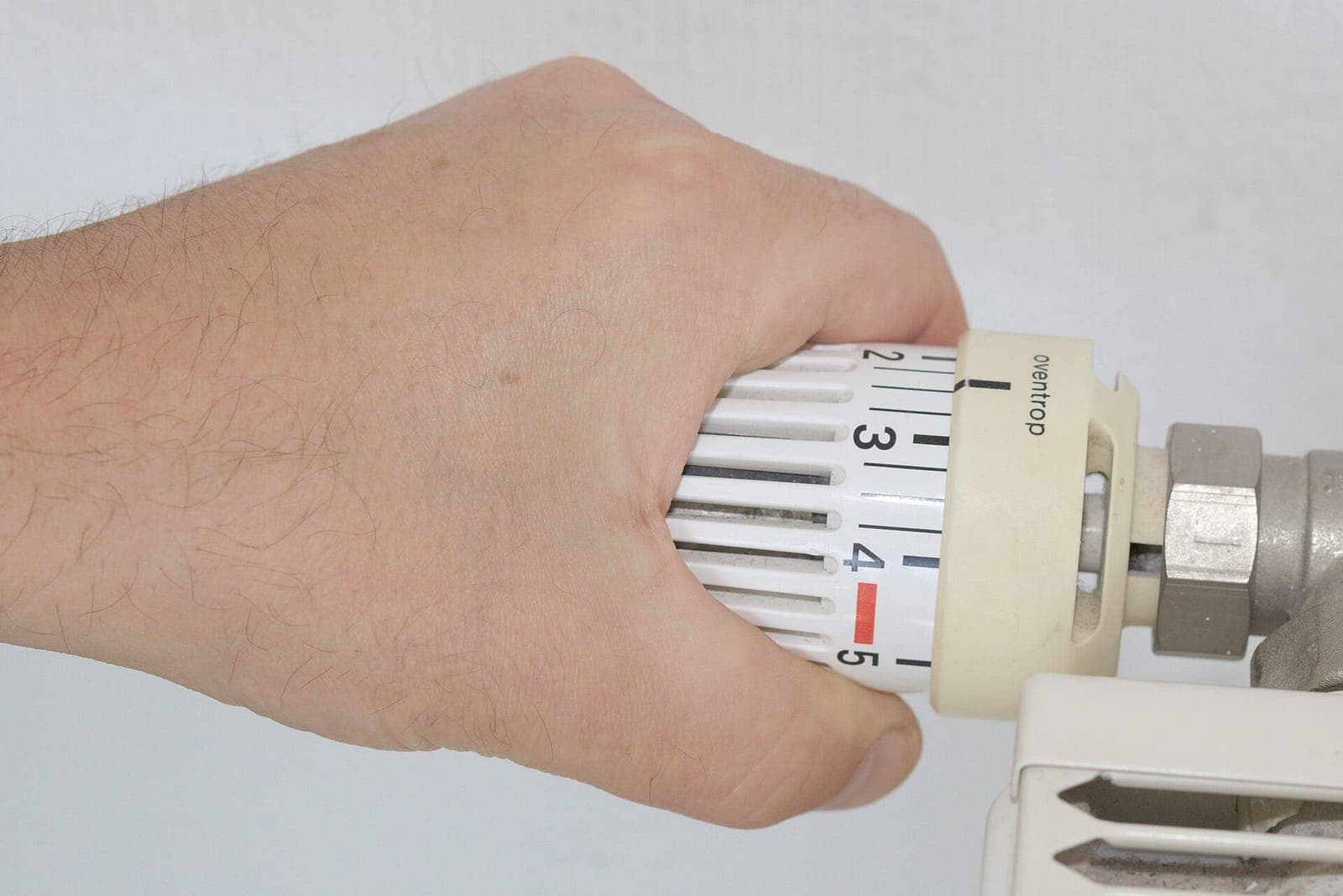 Eine Hand dreht am Thermostatventil eines Heizkörpers